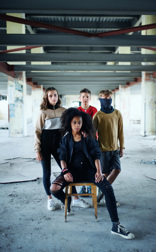 Front view of group of teenagers gang standing indoors in abandoned building, looking at camera.