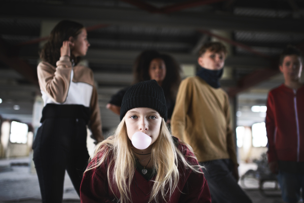 Portrait of teenager girl with friends standing indoors in abandoned building, making bubble gum.