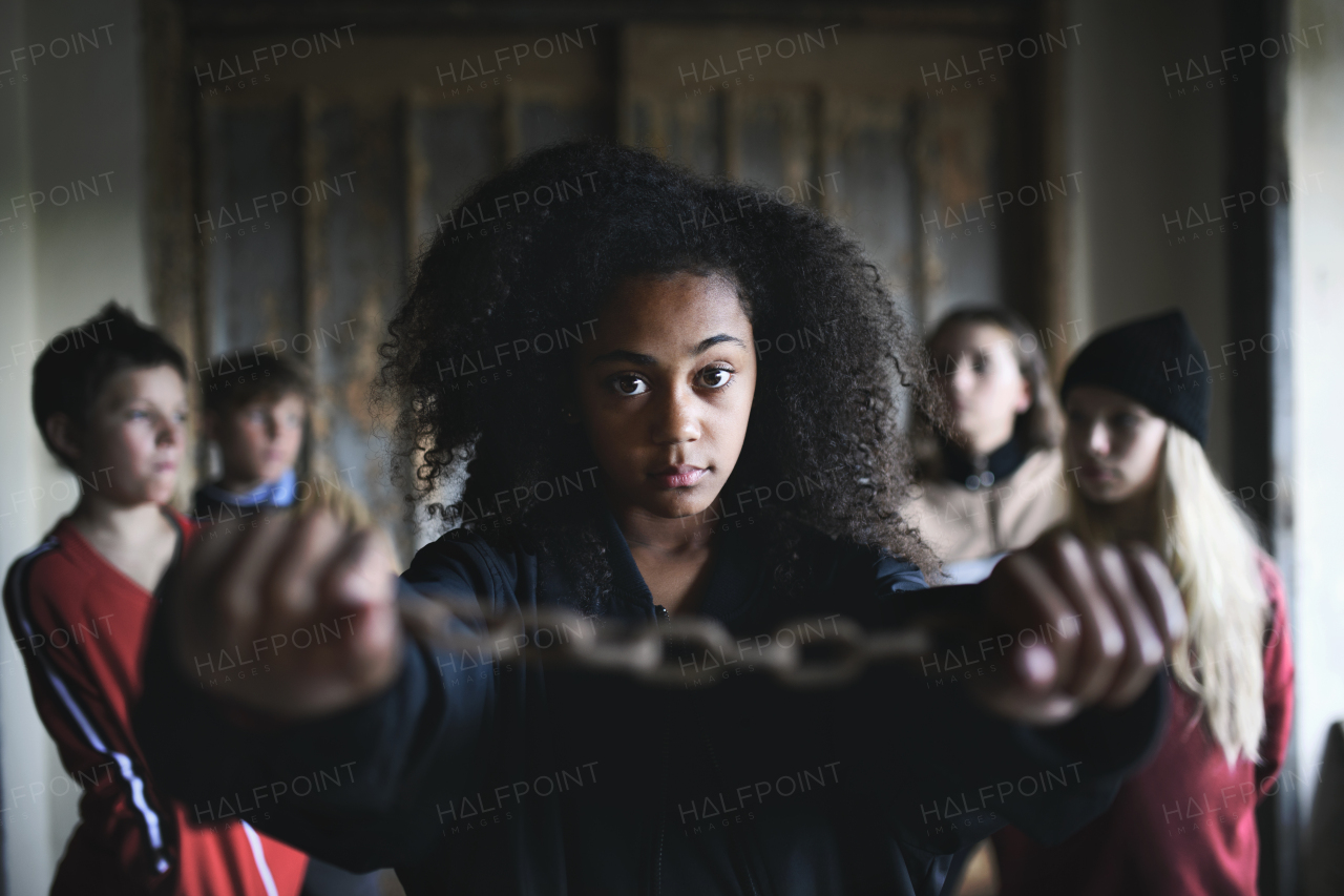 Front view portrait of mixed- race teenager girl with hands in chains and friends standing indoors in abandoned building.