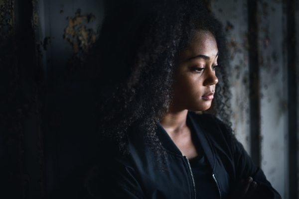 Side view portrait of sad mixed- race teenager girl standing indoors in abandoned building.