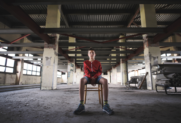 Sad and disappointed teenagers boy sitting on chair indoors in abandoned building.