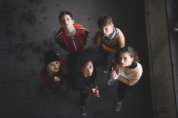 Top view of group of teenagers gang with lollipops standing indoors in abandoned building, looking at camera.