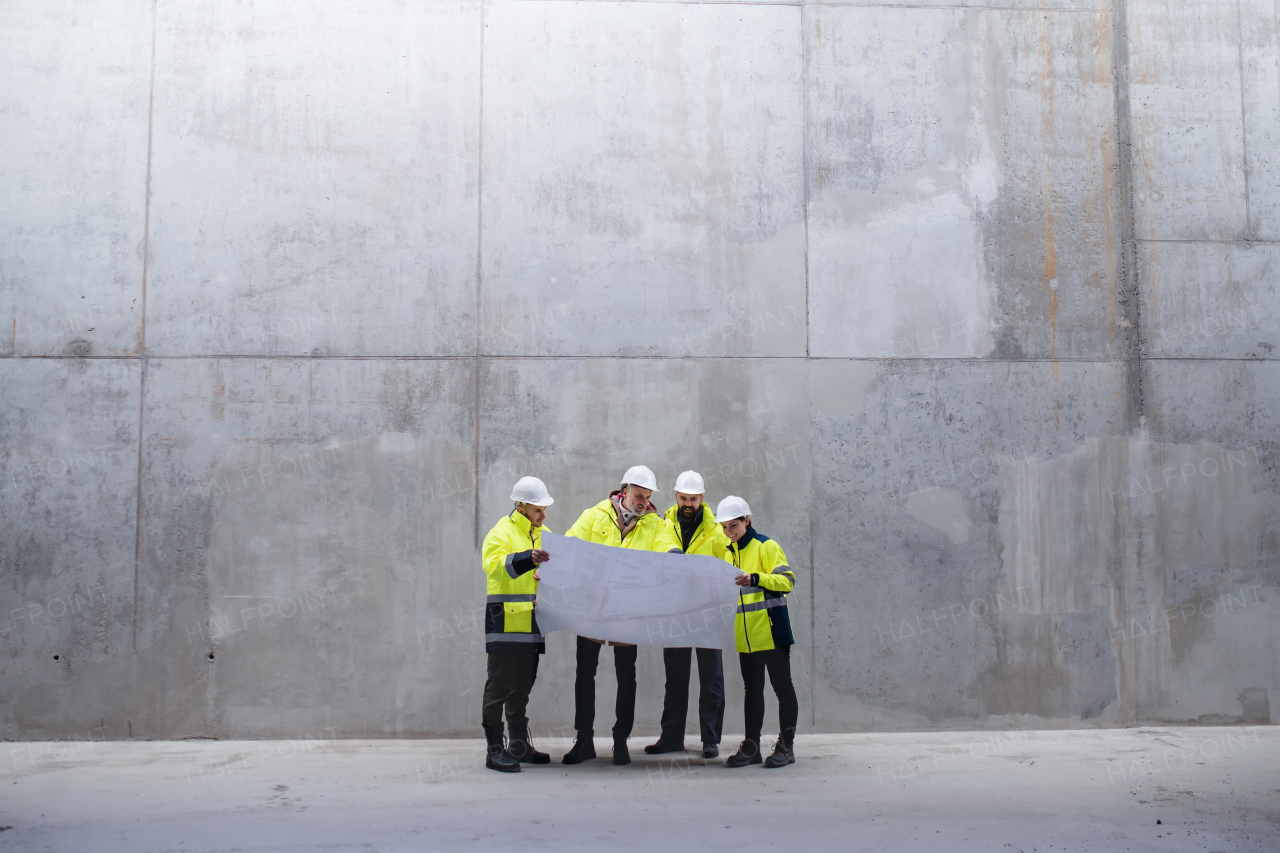 A group of engineers standing against concrete wall on construction site, holding blueprints. Copy space.