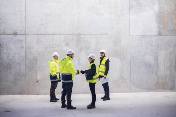 Group of engineers standing on construction site, shaking hands. Copy space.