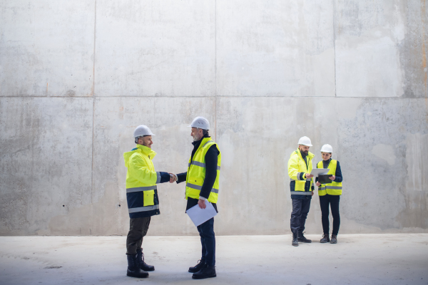 A group of engineers standing on construction site, shaking hands. Copy space.