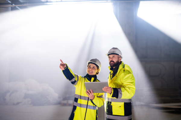 Engineers standing and talking outdoors on construction site, holding tablet.