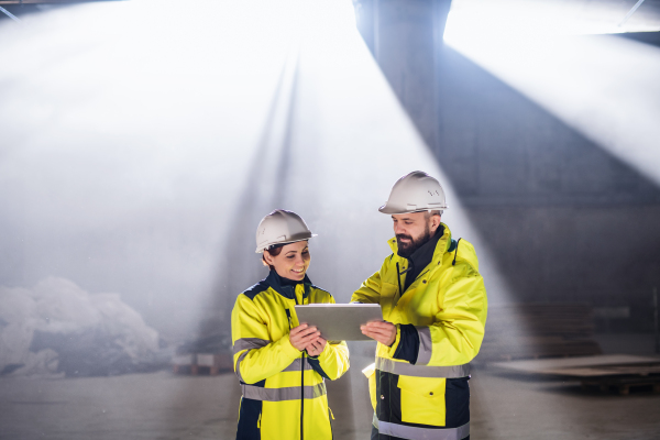 Engineers standing and talking outdoors on construction site, holding tablet.