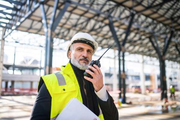 Man engineer using walkie talkie outdoors on construction site.