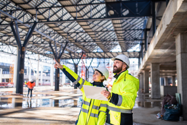 Engineers standing and talking outdoors on construction site, holding tablet.