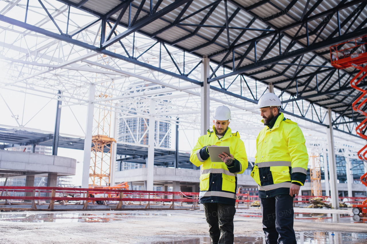 Men engineers standing outdoors on construction site, using tablet. Copy space.