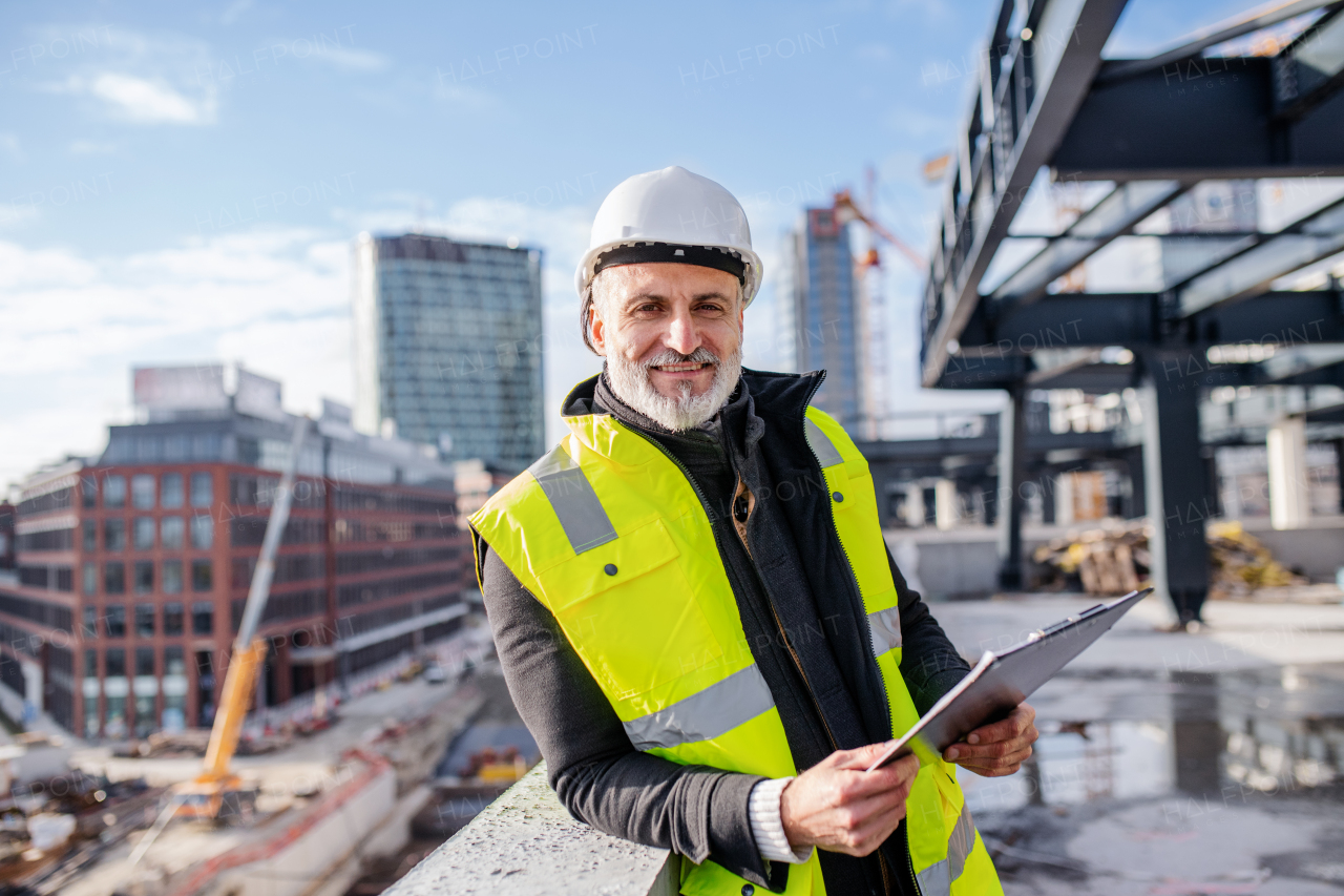 A man engineer standing outdoors on construction site, looking at camera.