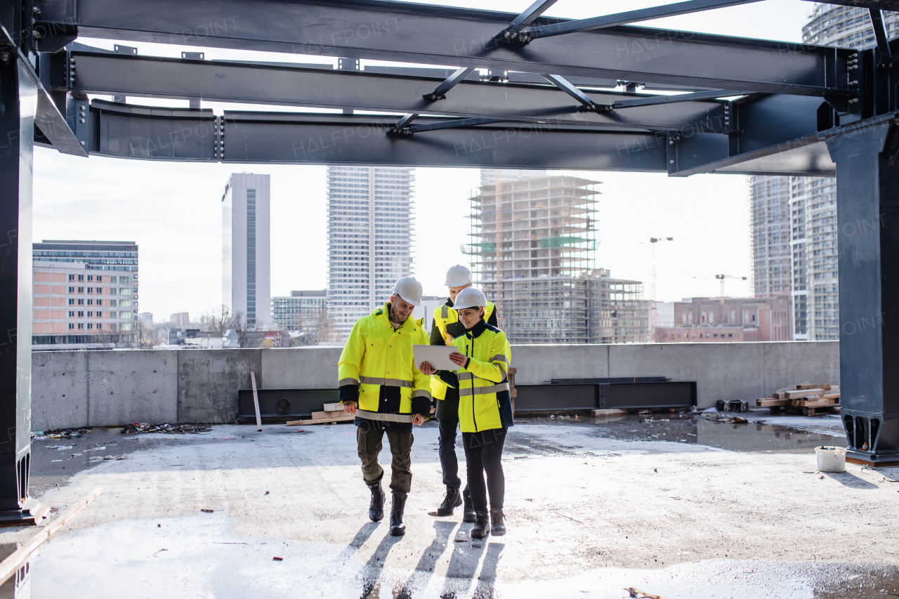 A group of engineers standing outdoors on construction site, using tablet.