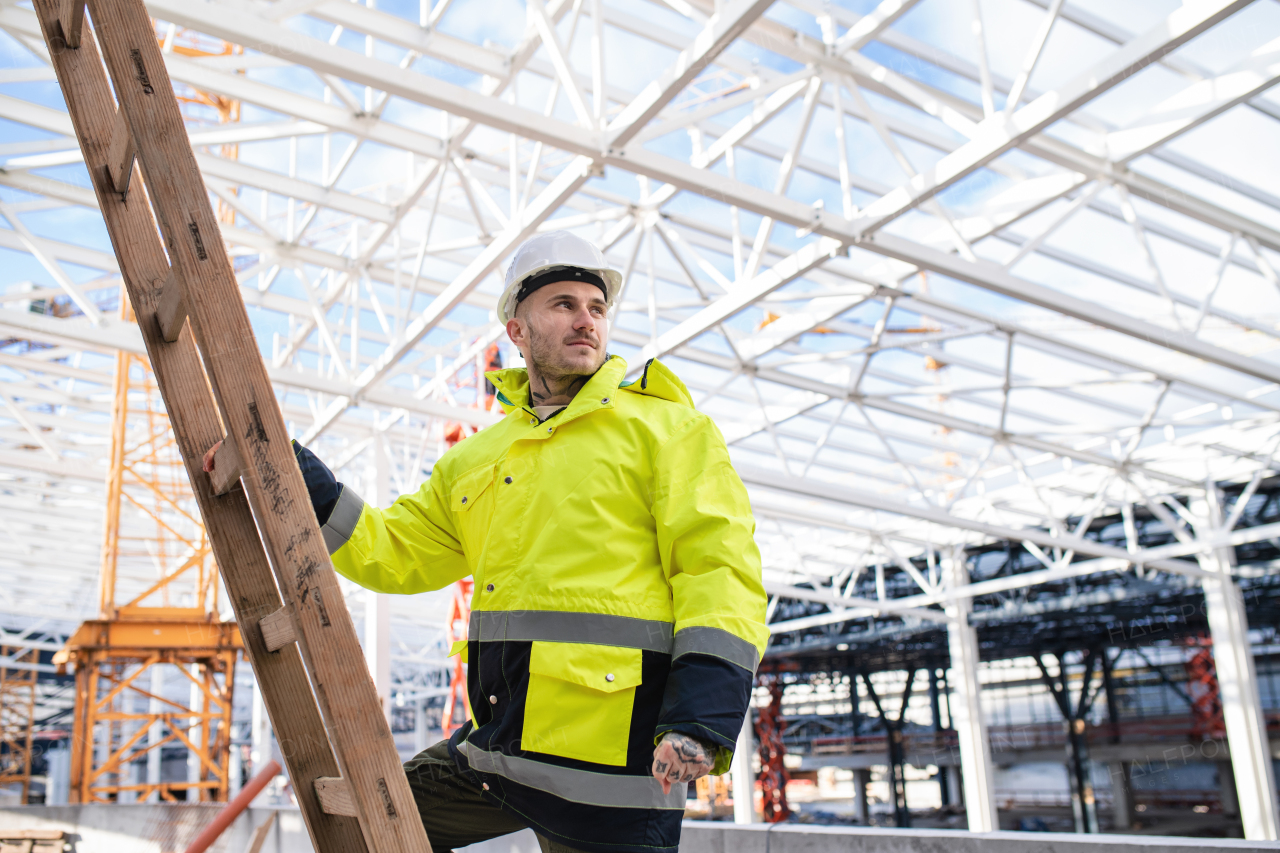 A young man worker outdoors on construction site, working.