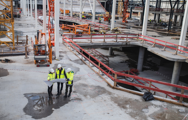 A top view of group of unrecognizable engineers with blueprints standing on construction site.