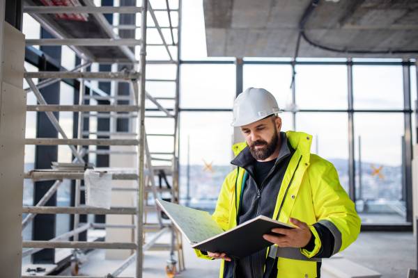 Mature man engineer standing on construction site, holding blueprints.