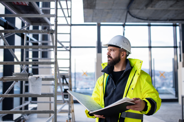 Mature man engineer standing on construction site, holding blueprints.