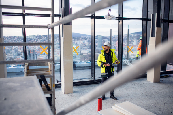 Mature man engineer standing on construction site, holding blueprints.