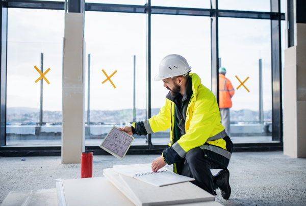 Mature man engineer with tablet on construction site, looking at blueprints.