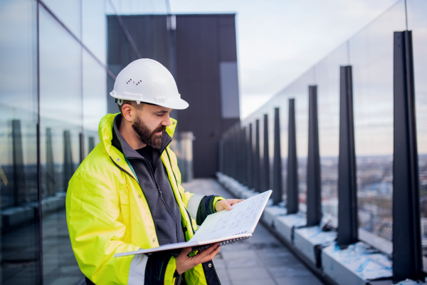 Mature man engineer standing on construction site, holding blueprints.