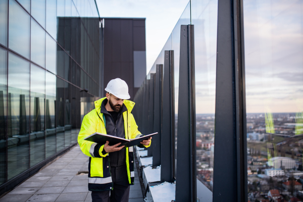 Mature man engineer standing on construction site, holding blueprints.