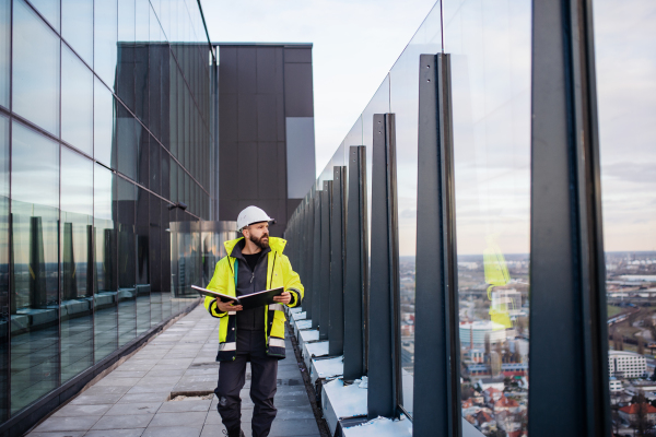 Mature man engineer walking on construction site, holding blueprints.