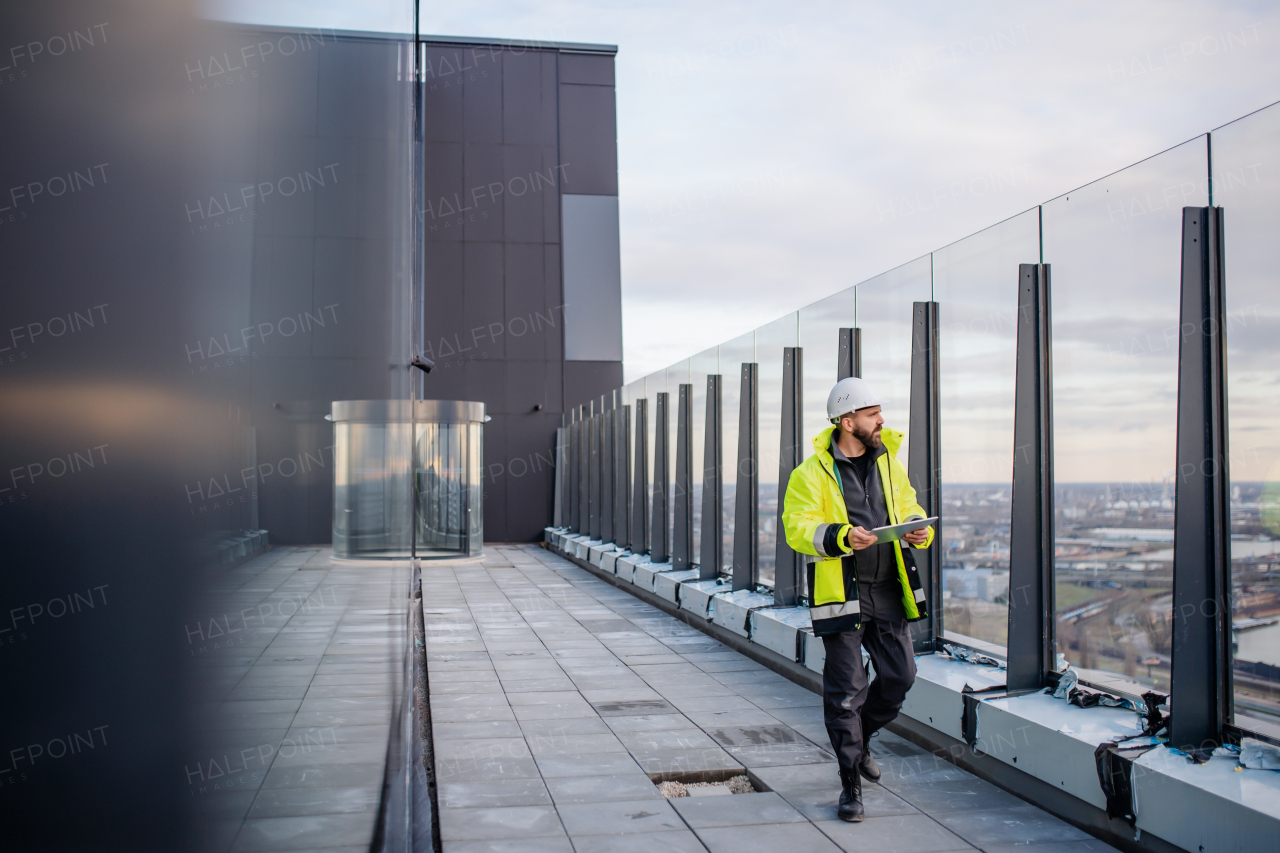 Mature man engineer walking on construction site, holding tablet with blueprints.