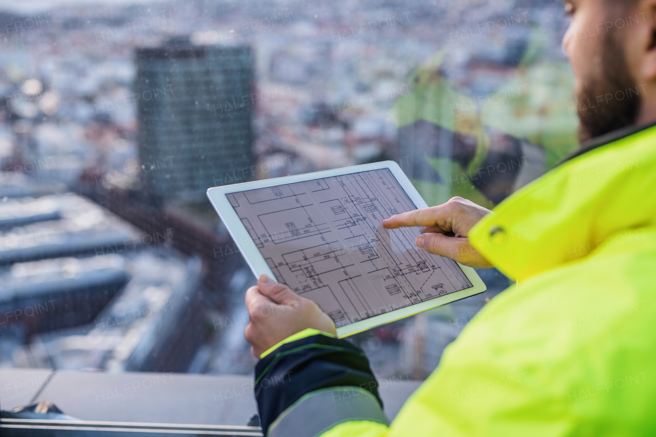 Midsection of unrecognizable man engineer with tablet on construction site, looking at blueprints.