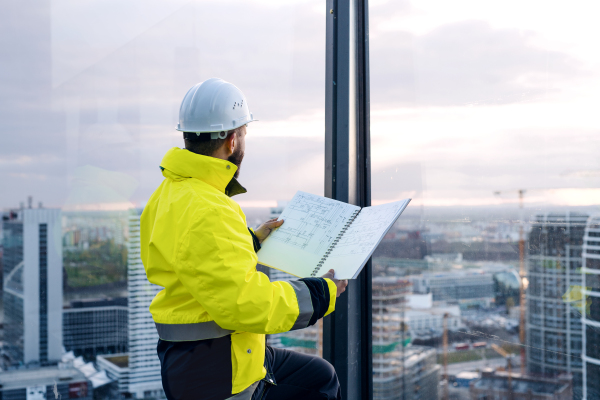 Mature man engineer standing on construction site, holding blueprints.