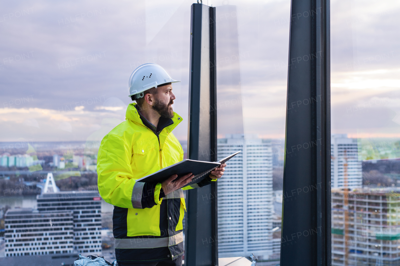 Mature man engineer standing on construction site, holding blueprints.