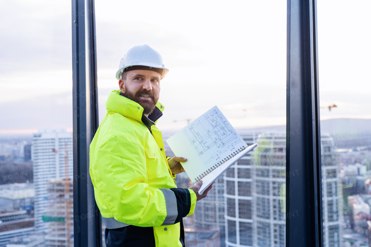 Mature man engineer standing on construction site, holding blueprints.