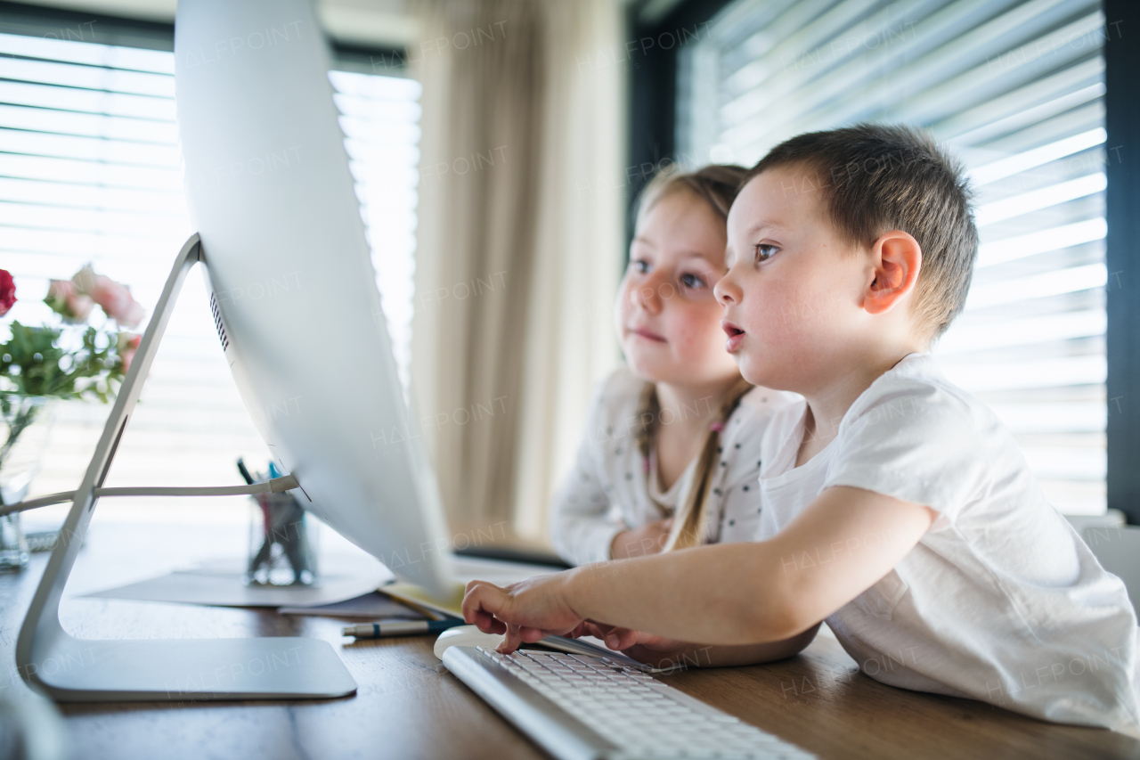 Small girl and boy sitting at the table, using computer indoors at home. Corona virus and quarantine concept.