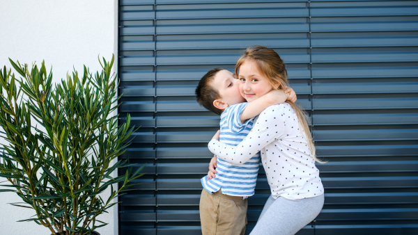 Small girl and boy standing outdoors at home, hugging. Corona virus and quarantine concept.