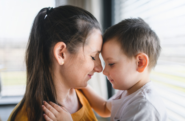 Side view of mother and child indoors at home, hugging.