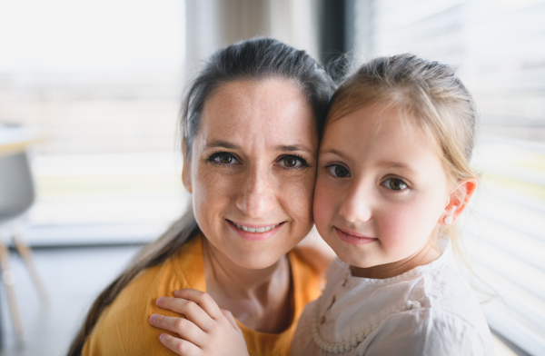 Front view of mother and child indoors at home, looking at camera.