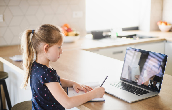 Small girl with laptop learning through internet indoors at home, Corona virus and quarantine concept.