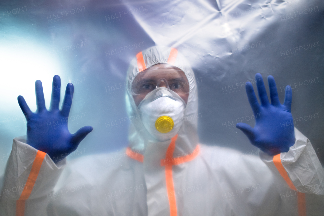 Front view of man with protective suit and respirator indoors, coronavirus concept.