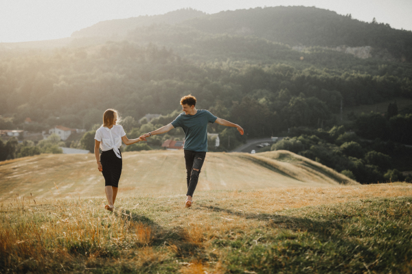 Front view of young couple walking in nature at sunset in countryside, holding hands.