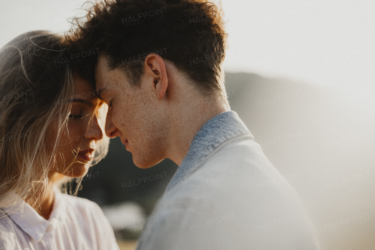 Side view of young couple on a walk in nature at sunset in countryside, hugging.