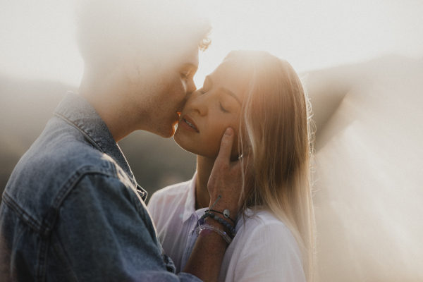 Side view of young couple on a walk in nature at sunset in countryside, kissing.