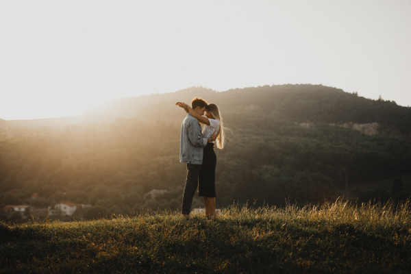 Side view of young couple on a walk in nature at sunset in countryside, hugging.