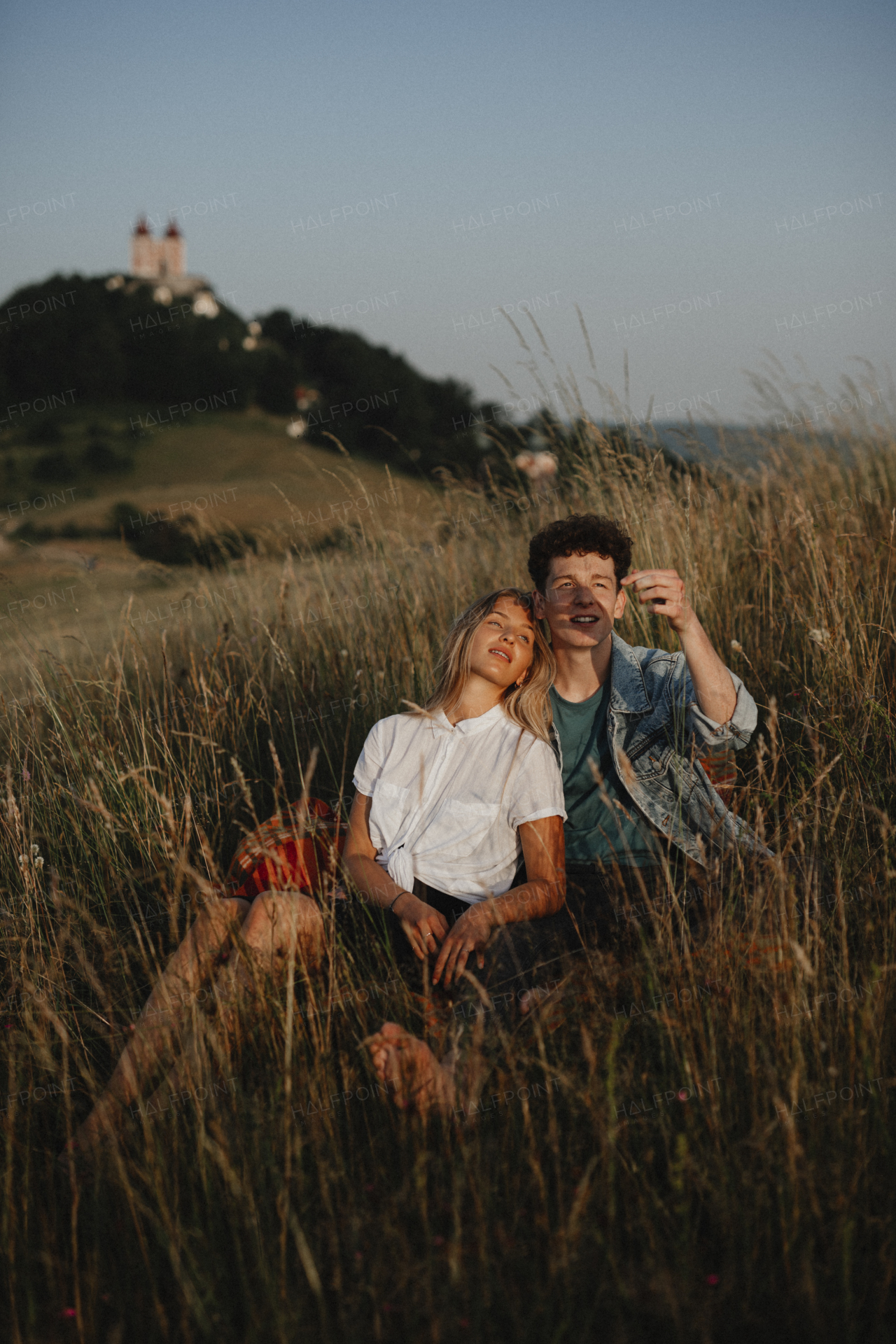 A young couple on a walk in nature at dusk in countryside, sitting and resting in long grass.