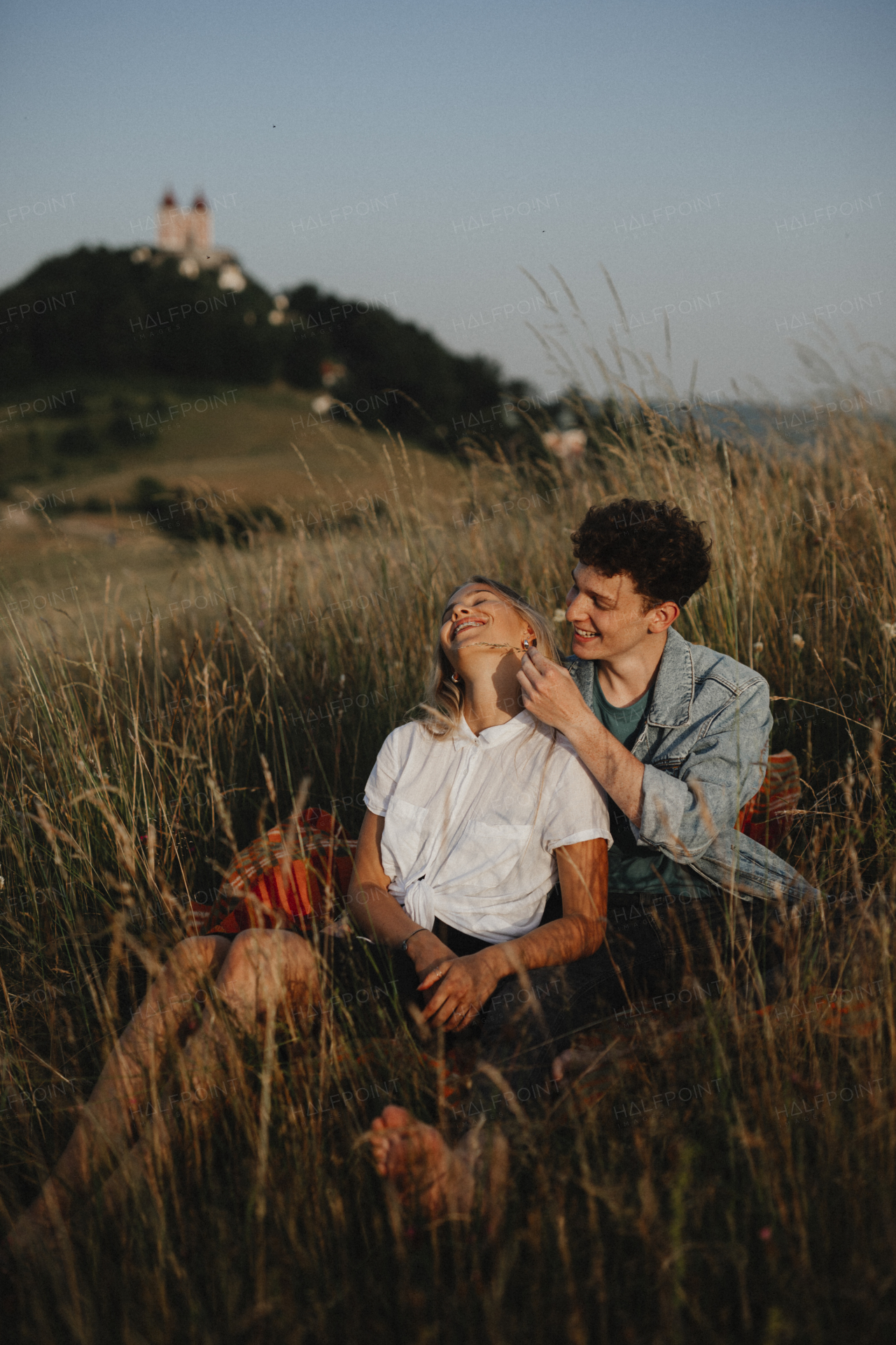 A young couple on a walk in nature at dusk in countryside, sitting and resting in long grass.