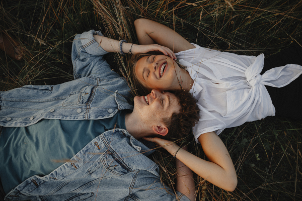 A young couple on a walk in nature in countryside, lying in grass laughing.