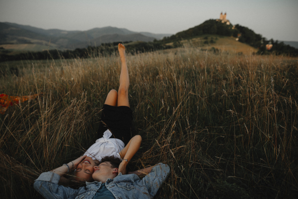 A young couple on a walk in nature in countryside, lying in grass laughing.