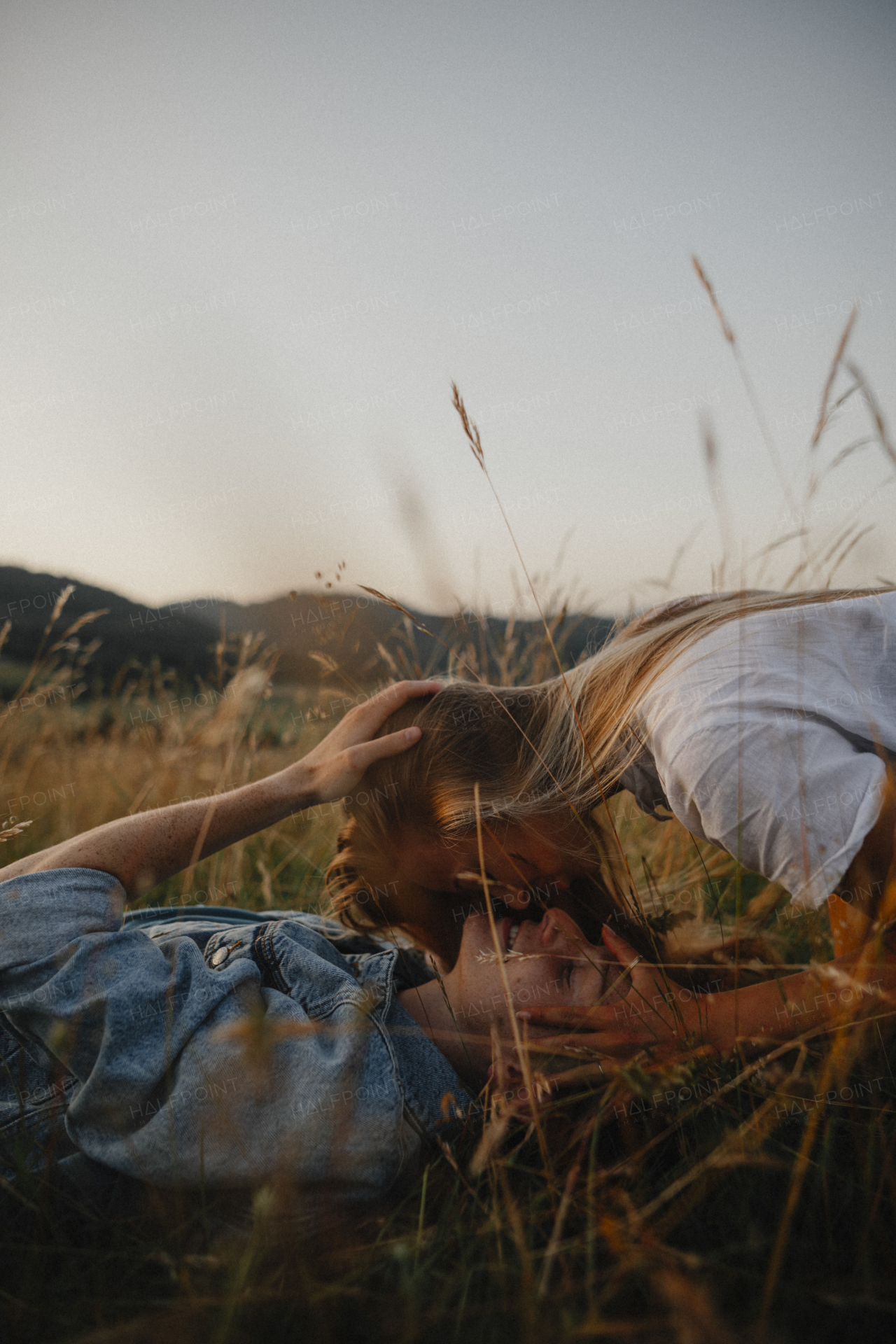 A young couple on a walk in nature in countryside, lying in grass kissing.