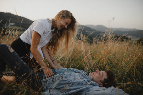 A young couple on a walk in nature in countryside, lying in grass laughing.