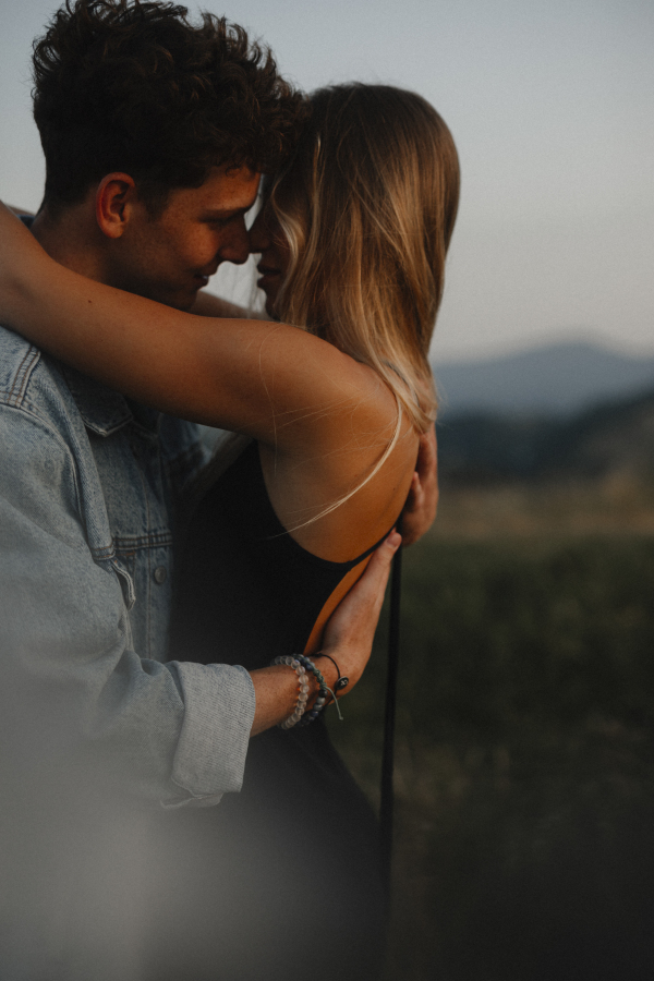 Side view of young couple on a walk in nature at sunset in countryside, hugging.