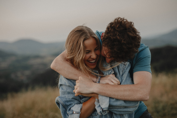 Side view of young couple on a walk in nature at sunset in countryside, hugging and having fun.