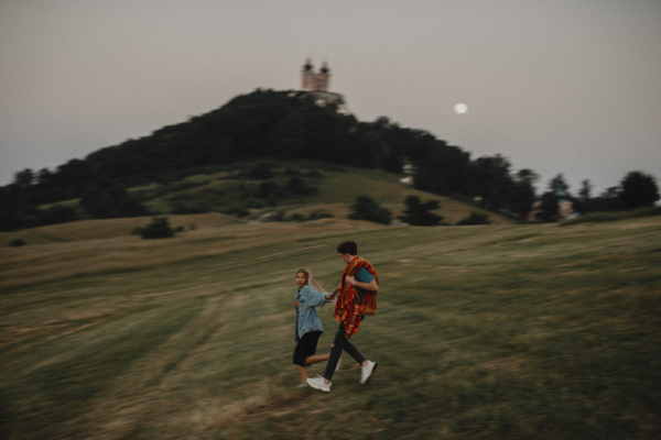 Front view of young couple walking in nature at sunset in countryside, holding hands and running.