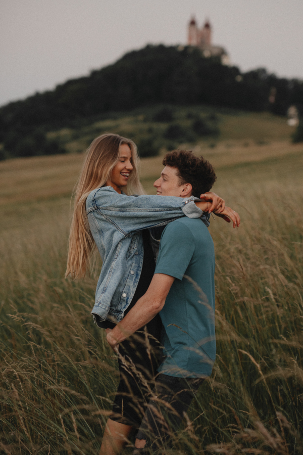 Side view of young couple on a walk in nature at sunset in countryside, hugging.